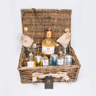 Ultimate gin hamper featuring 70cl bottle, mini bottles, mixers, garnishes, and branded glasses in a wicker basket